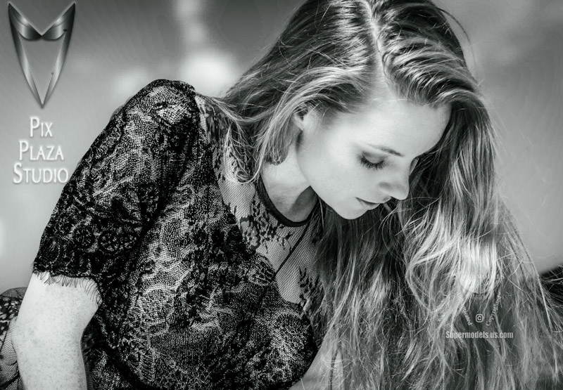 young woman wearing black lace nightgown leaning on her left arm and looking down in boudoir pose